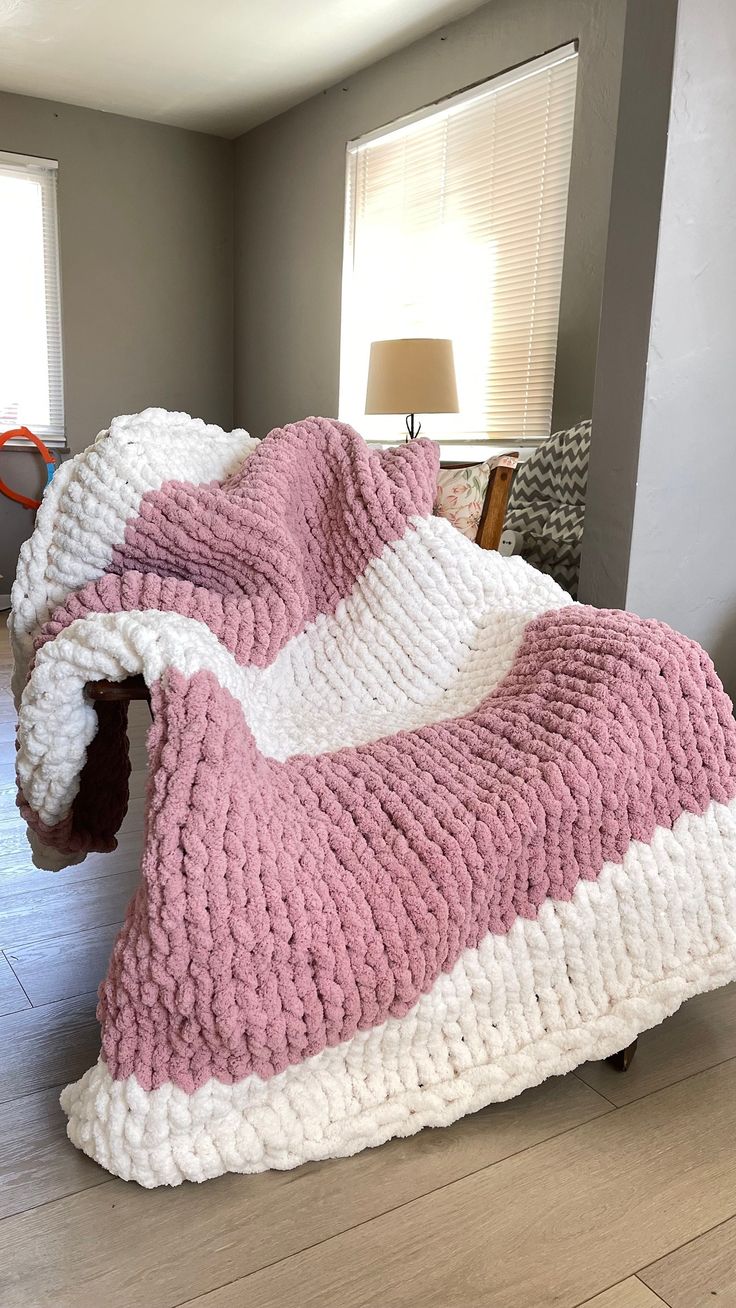 a large pink and white blanket on top of a wooden floor next to a lamp