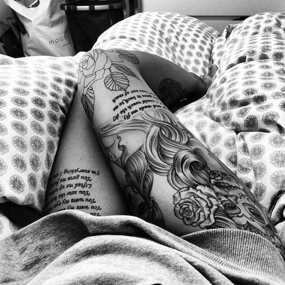 a woman laying in bed with tattoos on her arm and leg, reading a book