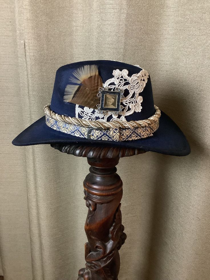 This is a custom weathered hat with incredible detail.  Navy felt hat with blue and cream woven hat band.  Additional rope in cream.  Lace appliqués on each side.  Genuine turkey feather.  Vintage picture frame.  Fuzzy light blue balls for decoration.  Adjustable band inside to fit any size. Handmade Vintage Mini Fedora, Handmade Vintage Hat Bands For Kentucky Derby, Handmade Vintage Fedora For Kentucky Derby, Blue Hat With Curved Brim For Country Events, Vintage Blue Hat With Curved Brim, Custom Blue Hat For Kentucky Derby, Vintage Handmade Hats For Country Events, Blue Country Hat With Short Brim, Blue Curved Brim Hat For Country Events