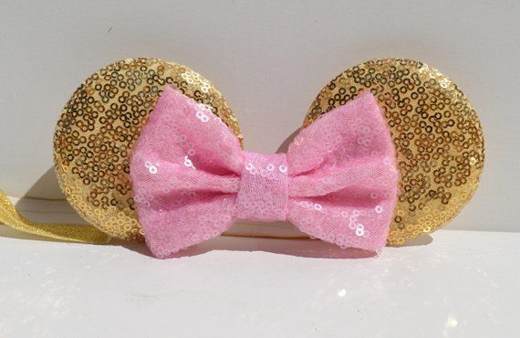 a pink and gold sequin minnie mouse ears with a bow on the side, sitting on a white surface