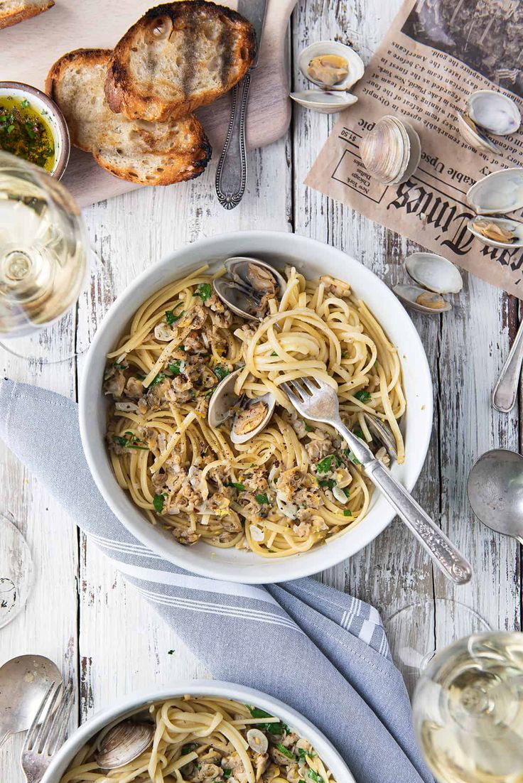 two bowls of pasta with mushrooms and parmesan bread on the side next to wine glasses