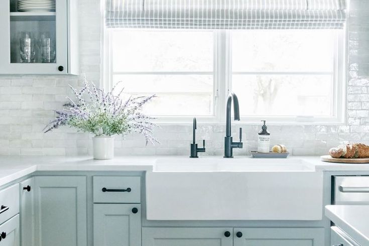 a kitchen with white cabinets and gray counter tops, along with a window over the sink