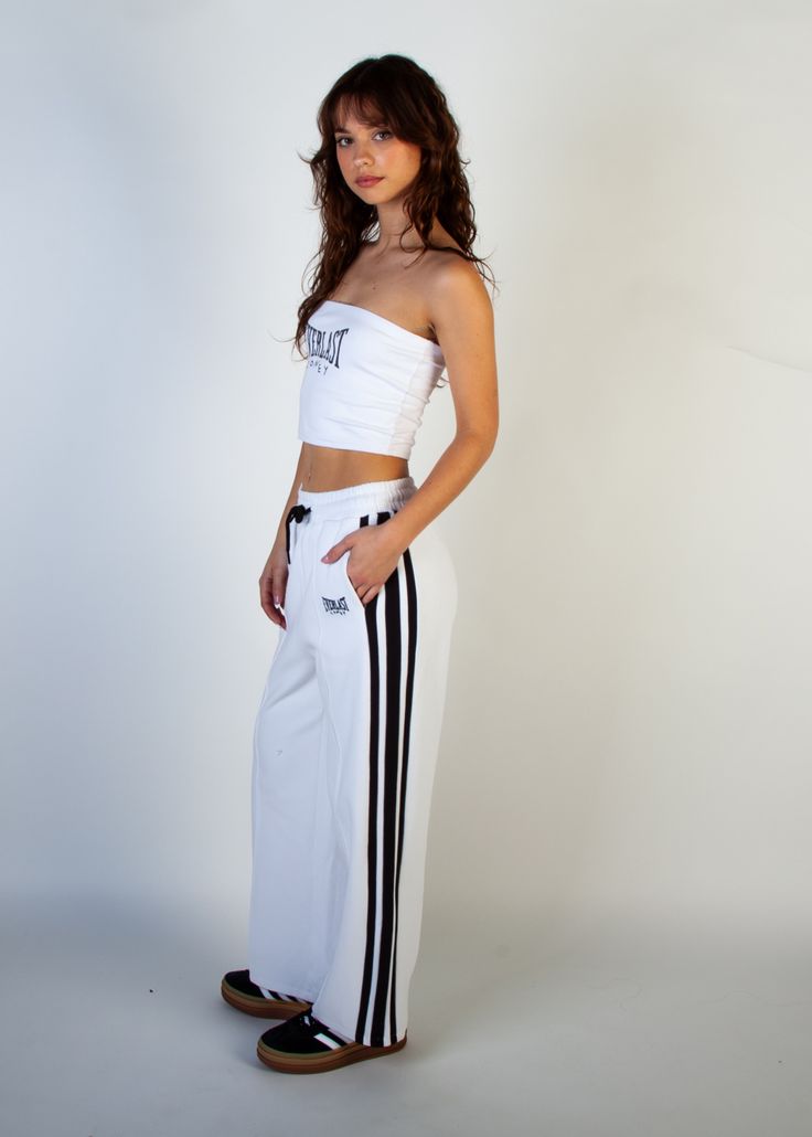 Embrace the fusion of retro aesthetics and contemporary comfort with our women's Everlast x Coney Wide Leg Track Pant. These track pants are designed for both style and functionality, featuring a wide-leg silhouette that pays homage to vintage sportswear while ensuring a modern fit. With contrast side stripes and pintuck details, they effortlessly infuse your look with athletic flair. Complete with iconic collaboration embroidery at the hip, these high-waisted pants offer the perfect blend of no Trendy White Sports Bottoms, White Full Length Sweatpants For Sports, Sporty Wide Leg Pants For Streetwear, White Wide-leg Sweatpants For Streetwear, White Wide Leg Trousers For Streetwear, Sporty White Sweatpants With Side Stripes, Trendy White Sweatpants For Sports, Trendy White Sweatpants For Streetwear, White Full-length Sporty Bottoms