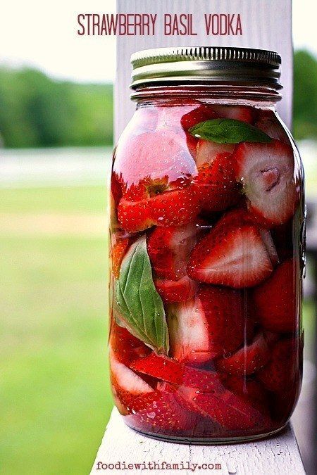 a jar filled with sliced strawberries on top of a wooden table next to grass