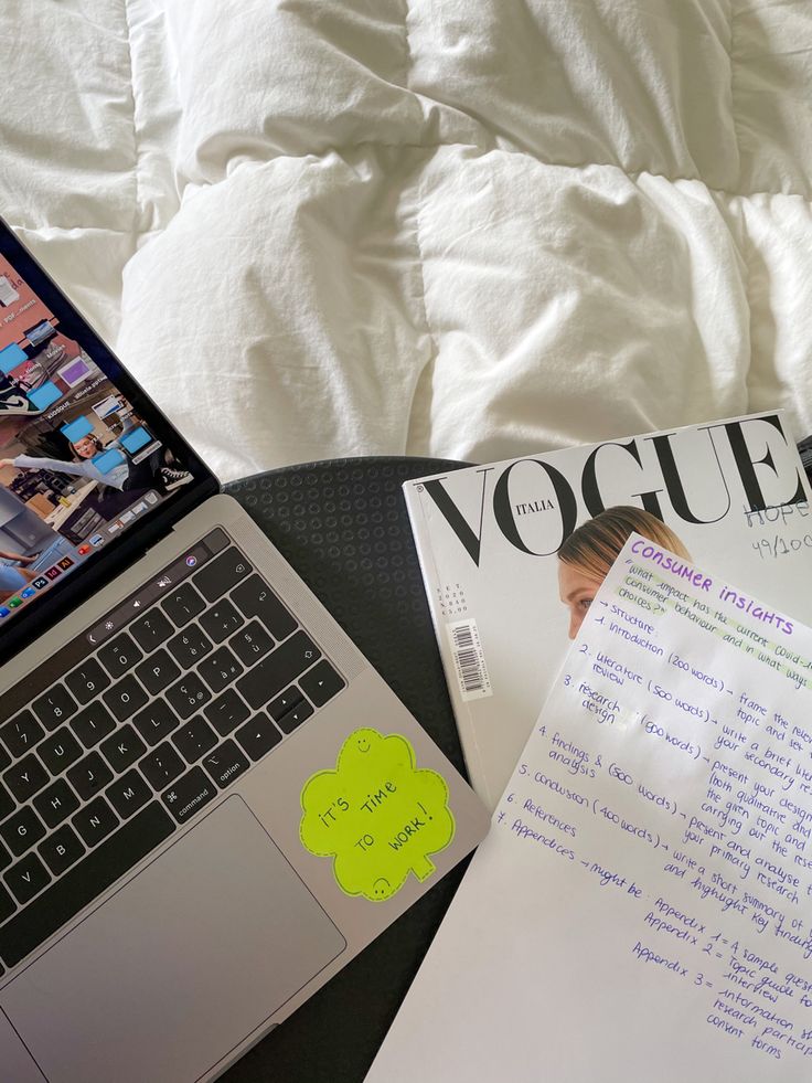 an open laptop computer sitting on top of a bed next to a notepad and paper