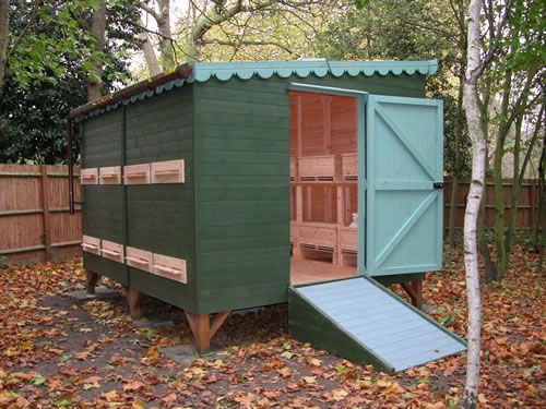 a small green shed sitting in the middle of a leaf covered yard next to a wooden fence