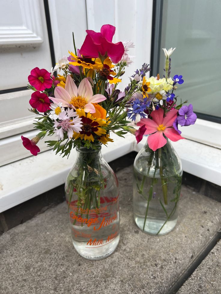 two glass vases with flowers in them sitting on a window sill next to each other