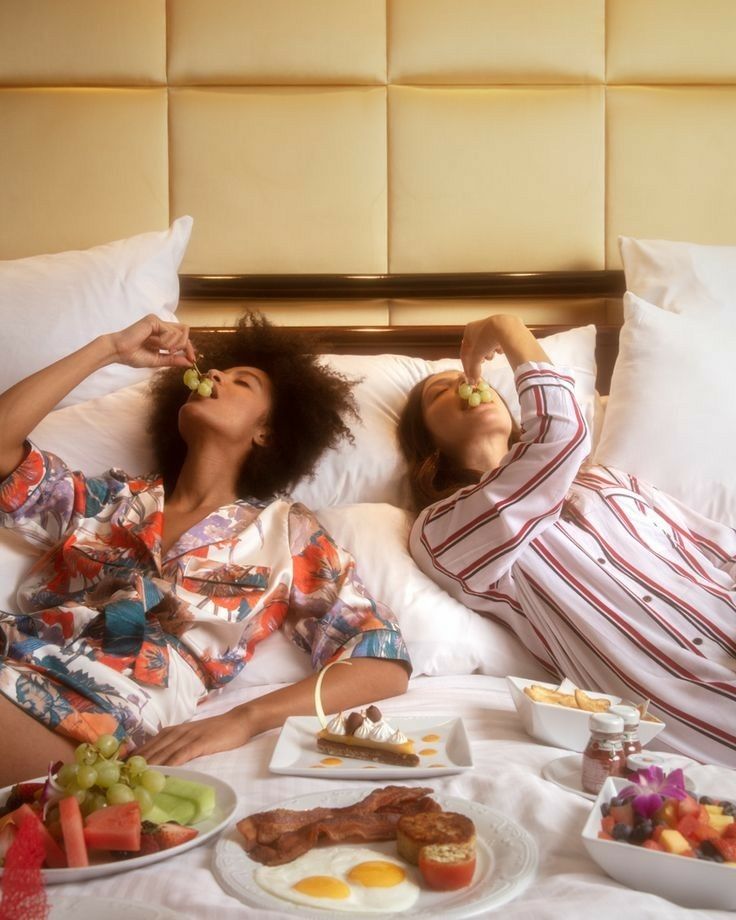 two people laying in bed with food and drinks