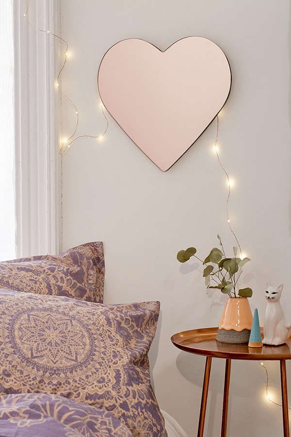 a heart shaped mirror hanging on the wall next to a table with pillows and vases