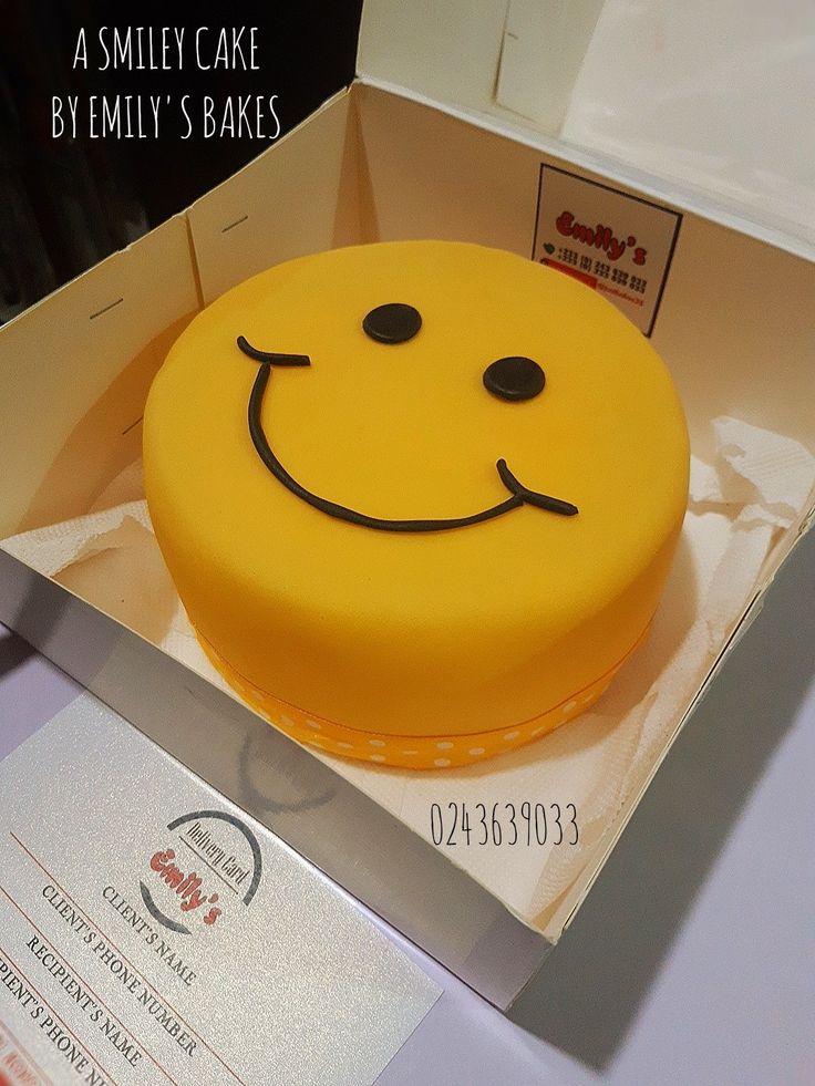 a smiley face cake in a box on a table with a business card behind it