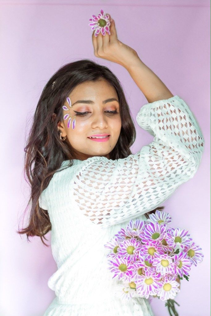 a woman with flowers in her hair and holding one flower up to her head while smiling at the camera