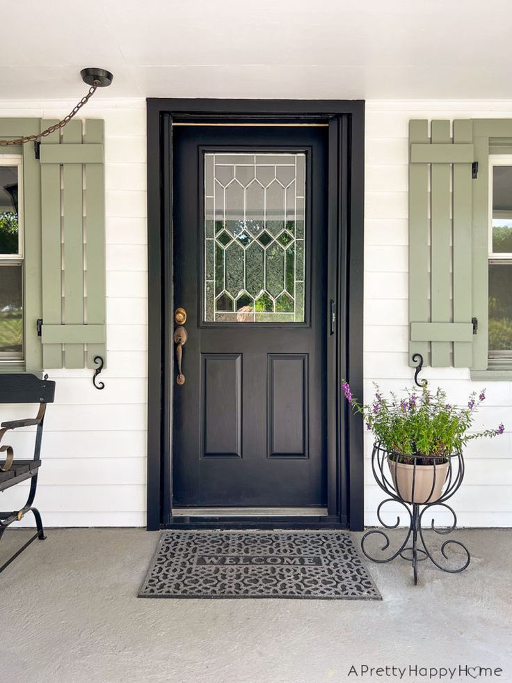 a black front door with green shutters and potted plants