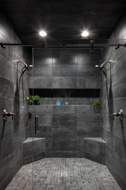 a walk in shower sitting next to a tiled wall and floor with plants on it