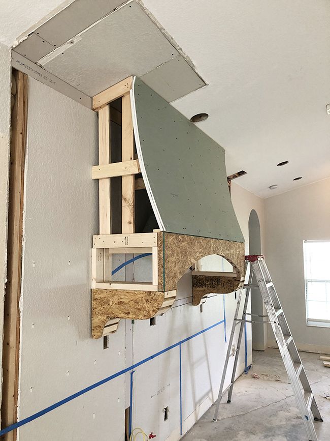 an unfinished room with a stove and ladder in the foreground, being worked on