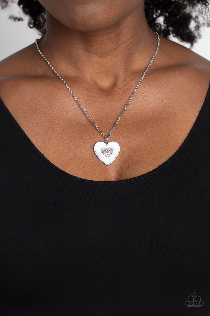 Painted in a shimmery white lacquer finish, a silver heart swings from the bottom of a dainty silver chain below the collar for a charming finish. Featured in the center of the white backdrop, a smaller heart, bedazzled with dainty white rhinestones, adds a spritz of glitz to the romantic design. Features an adjustable clasp closure.   Sold as one individual necklace. Includes one pair of matching earrings. White Heart Necklace For Wedding, White Heart-shaped Wedding Necklace, White Jewelry With Adjustable Chain For Valentine's Day, White Pendant Necklace For Valentine's Day, White Heart Necklace For Wedding On Valentine's Day, White Heart Charm Necklace For Wedding, White Pendant Jewelry For Valentine's Day, White Wedding Necklace With Heart Charm, White Silver Chain Jewelry For Wedding