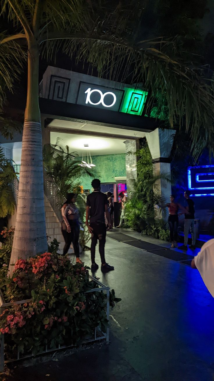 Shot of the entrance of the 100 restaurant in Kingston, Jamaica. With a palm tree and people in front Kingston Jamaica Aesthetic, Jamaica Restaurants, Jamaican Pictures, Jamaica Lifestyle, Aesthetic Jamaica, Jamaican Aesthetic, Jamaica Aesthetic, Jamaica Pictures, Caribbean Aesthetic