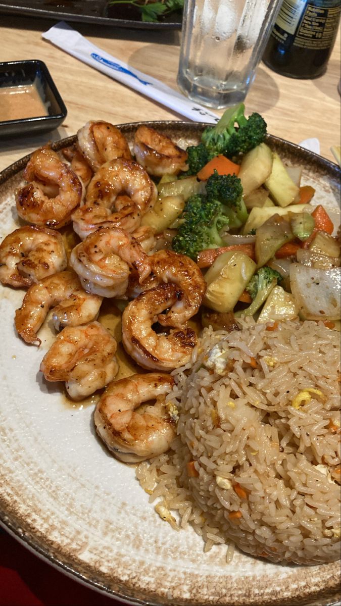 a plate with shrimp, rice and broccoli next to a glass of water