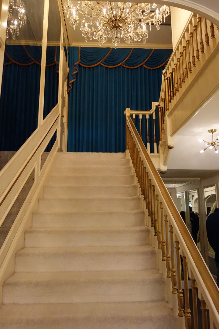 an elegant staircase with chandelier and blue curtains