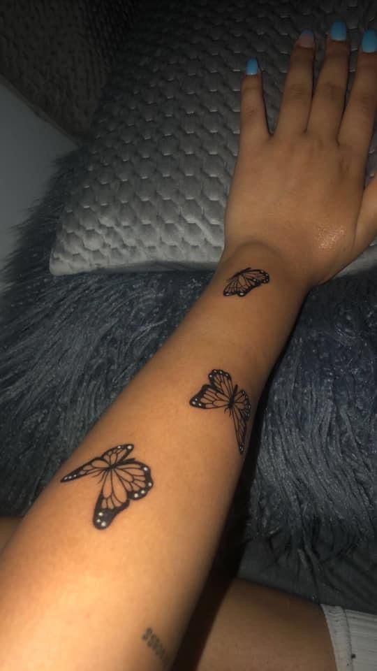 a woman's arm with butterflies on it and her hand resting on the pillow