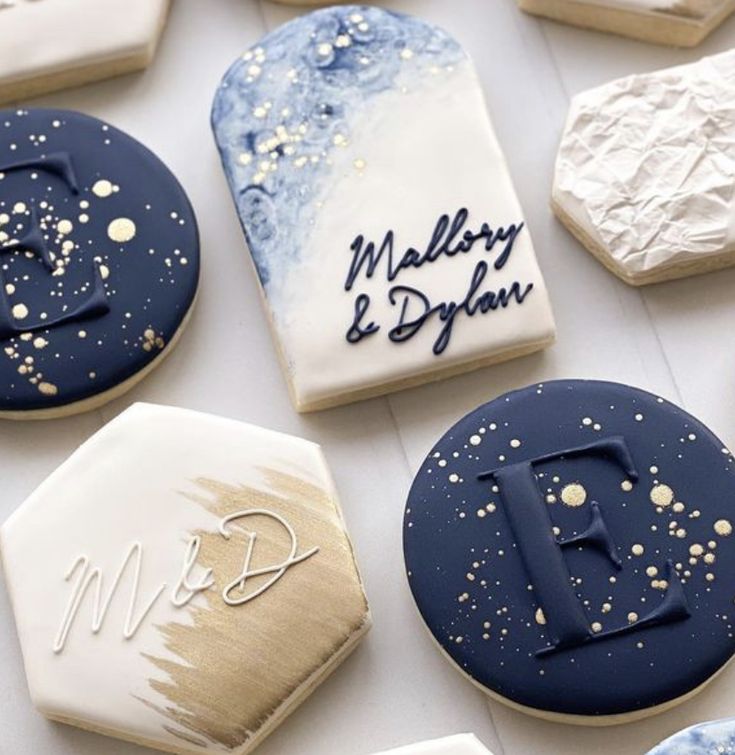 decorated cookies with blue and white frosting are arranged on a table top, including one for the letter d