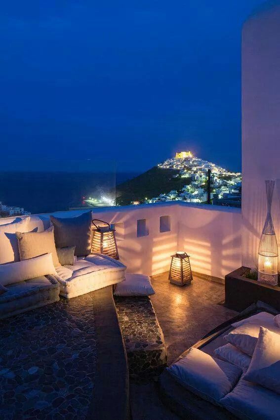 an outdoor living area with couches and lamps on the patio overlooking the ocean at night