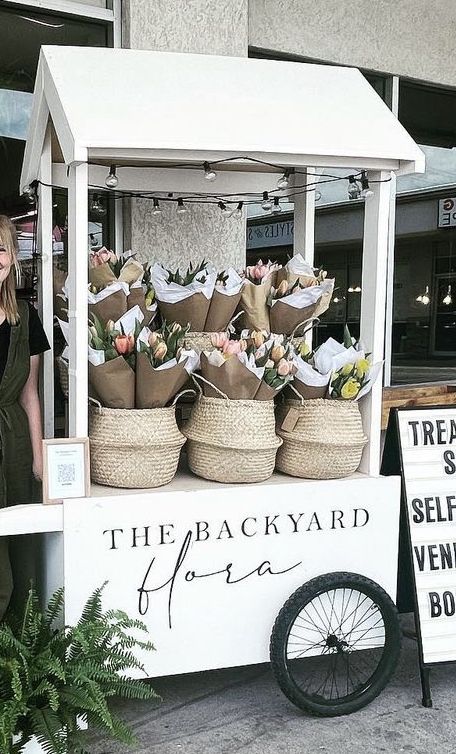 a woman standing in front of a stand with baskets on it's sides and a sign that says the backyard garden