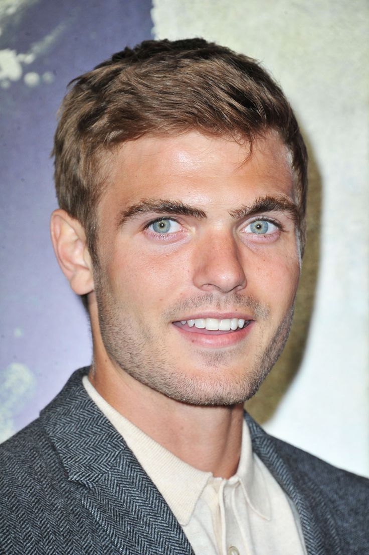 a close up of a person wearing a suit and smiling at the camera with blue eyes