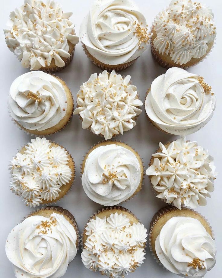 twelve cupcakes with white frosting and gold sprinkles on top