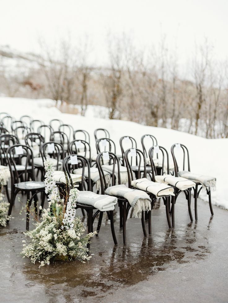 rows of black chairs sitting on top of a snow covered ground