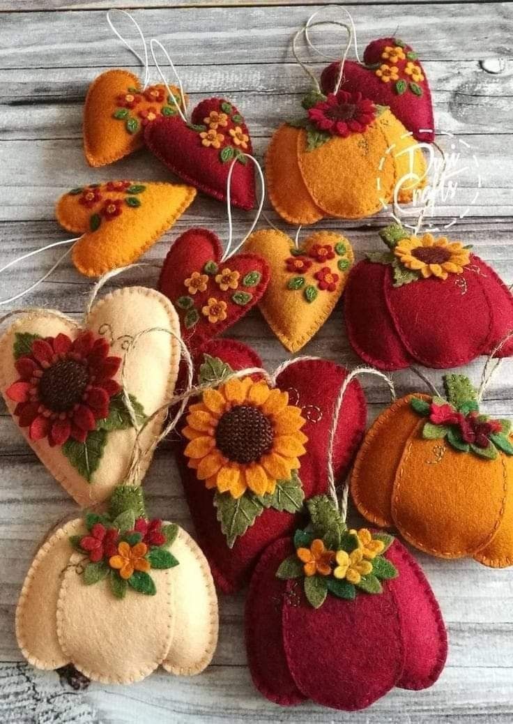 several felt pumpkins, sunflowers and hearts are hanging on a wooden table