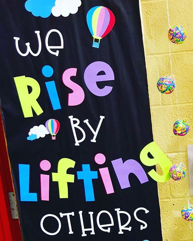 a sign that says we rise by lifting others up with balloons in the sky behind it