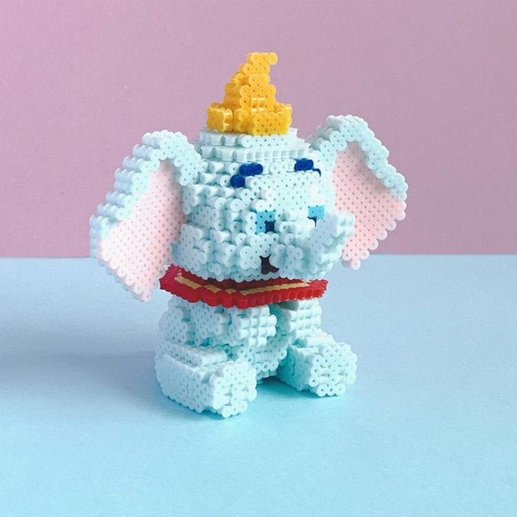 an elephant made out of legos with a crown on it's head, sitting in front of a pink background