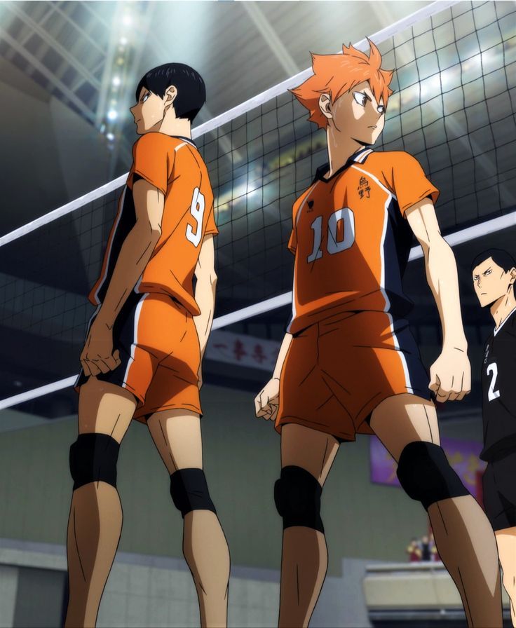 two men in orange uniforms standing next to each other near a volleyball net on an indoor court