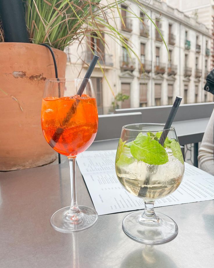 two wine glasses filled with drinks sitting on top of a table next to each other