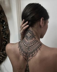 the back of a woman's neck with an intricate tattoo design on her left shoulder