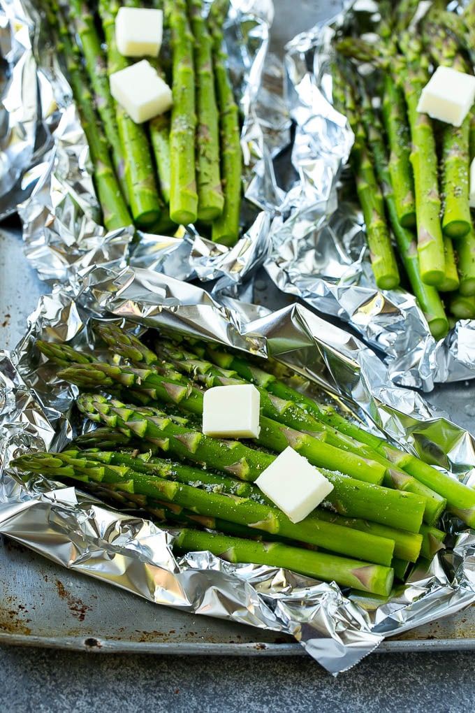 asparagus wrapped in aluminum foil with butter and garlic on the side, ready to be cooked