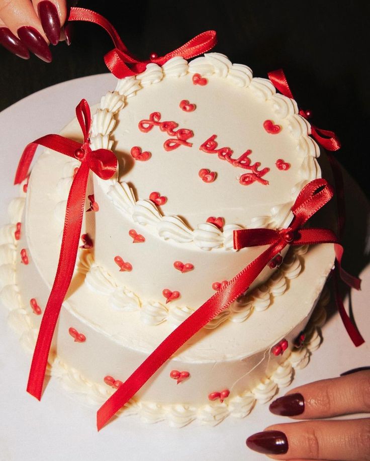 a white cake with red bows and the words baby on it is being held by a woman's hand