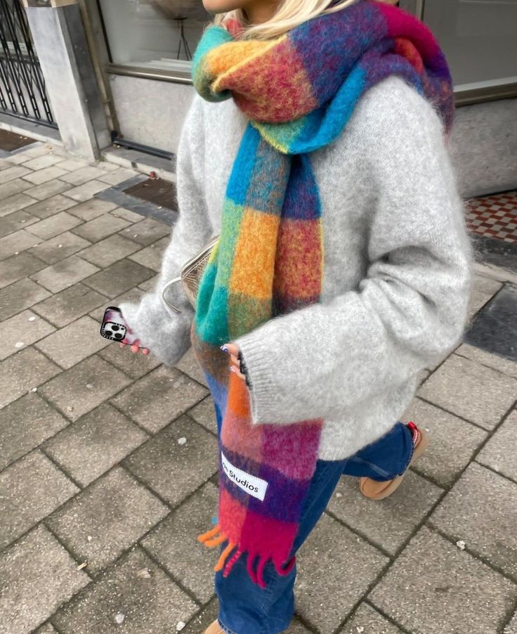 a woman with blonde hair wearing a multicolored scarf and hat on the sidewalk