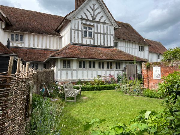 an old house with white and brown trim on the roof, surrounded by greenery