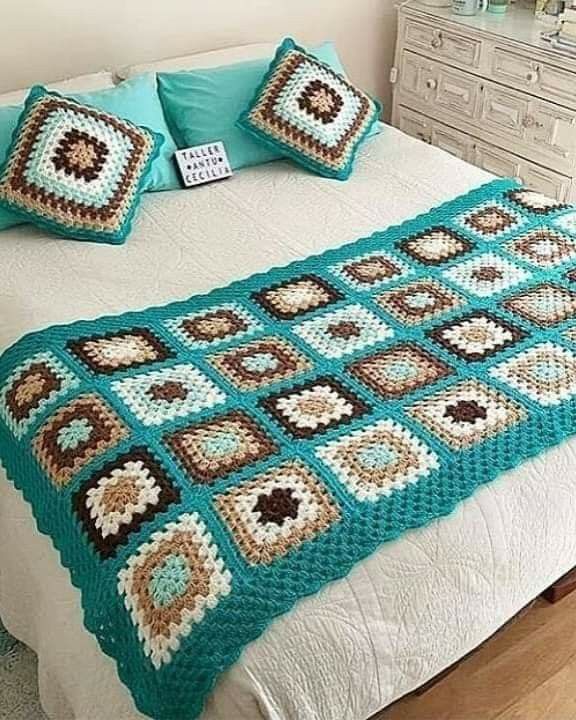 a crocheted blanket on top of a bed with two pillows in front of it