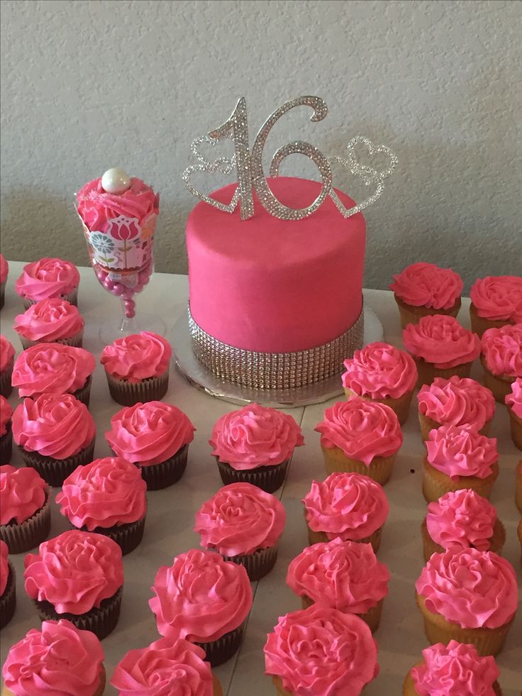 a table topped with pink frosted cupcakes next to a cake and candy container