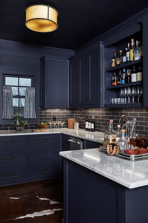 a kitchen with dark blue cabinets and white counter tops is lit by a pendant light