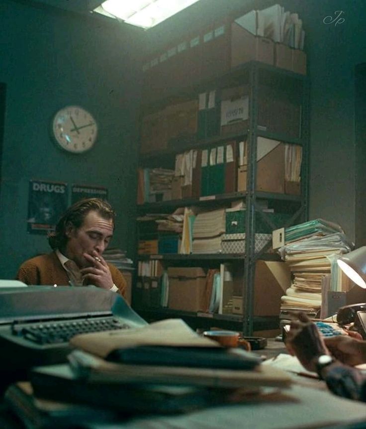 a man sitting at a desk in an office with stacks of papers on the table