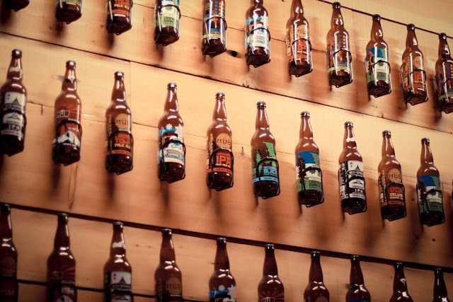 a wall full of beer bottles hanging on the side of a wooden wall next to each other