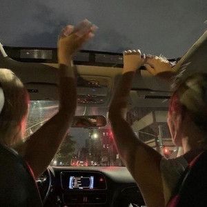 two people sitting in the back seat of a car with their hands up and one person wearing headphones