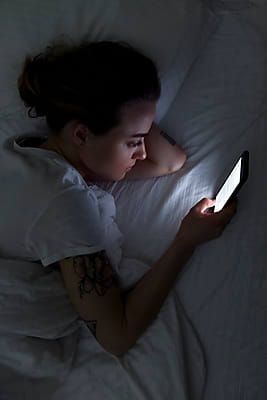 a woman laying in bed reading a book at night with the light shining on her