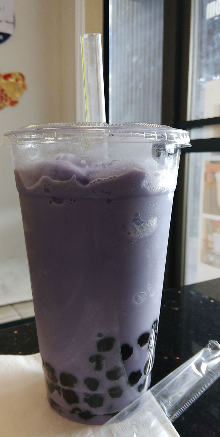 a purple drink sitting on top of a table next to a plastic cup with a straw in it