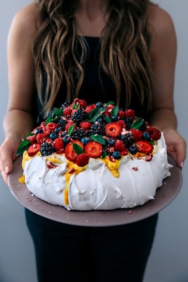 a woman holding a cake with fruit on top and frosting in the middle,