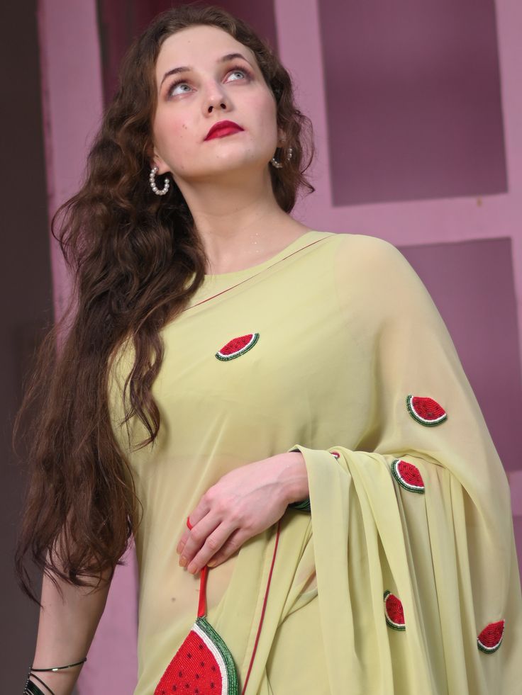 This is a three-piece watermelon saree set from the Ensembles collection. The pistachio green saree is paired with a matching sleeveless blouse. There are beautiful watermelon motifs of red, green, and white bead work all over the saree. This saree set is crafted in faux georgette fabric with contrast piping border. The outfit is completed with a heavily embellished, beadwork red, green and white watermelon shape handbag. Green Sharara With Traditional Drape For Summer, Green Traditional Drape Sharara For Summer, Green Sharara With Dupatta For Summer, Summer Semi-stitched Pre-draped Saree For Designer Wear, Bollywood Style Pre-draped Saree With Sheer Dupatta For Summer, Summer Festive Green Sharara, Summer Sharara With Unstitched Blouse In Georgette, Summer Designer Pre-draped Saree With Zari Work, Green Anarkali Sharara For Summer