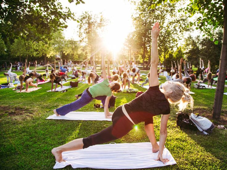 a group of people doing yoga on mats in a park with the sun behind them